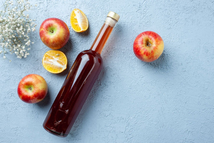 a bottle of apple cider vinegar along with some apples are kept on a table |  17 Apple Cider Vinegar Uses