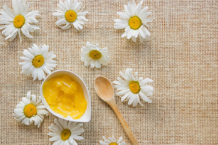 A bowl of butter kept along with spoon and flowers | Shea Butter for Skin