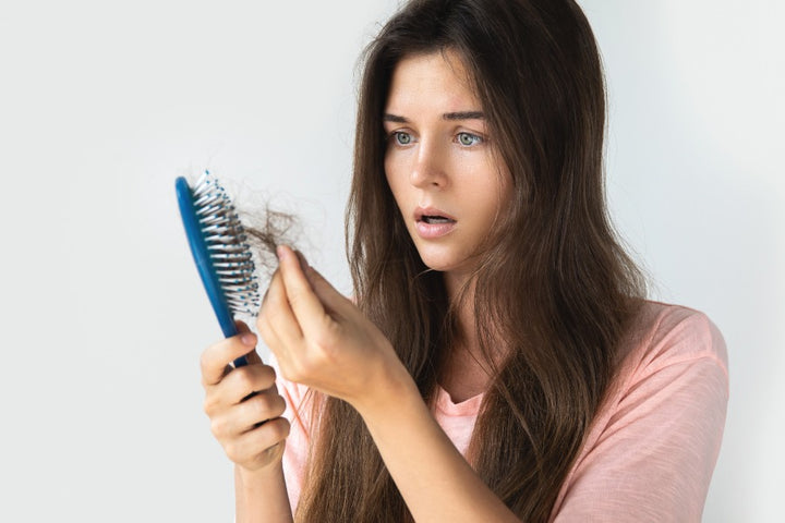 a woman suffering from extreme hair fall is looking at her comb filled with hair strands