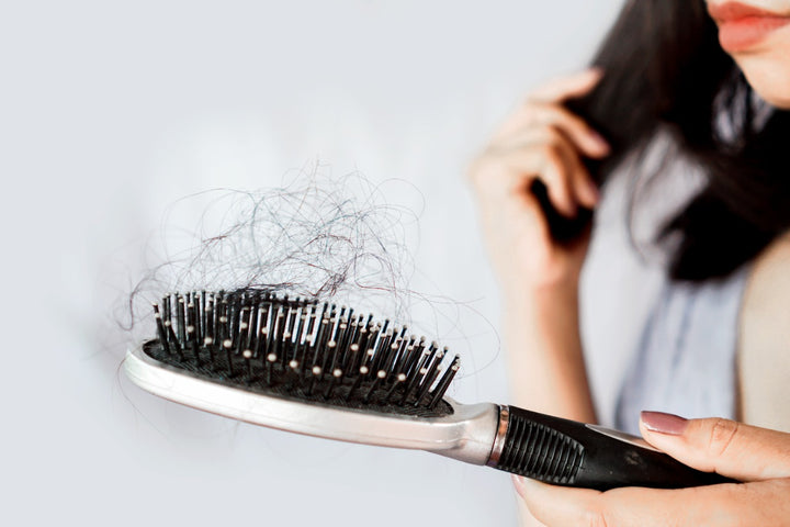 a woman holding a brush with a lot of hair stuck on it