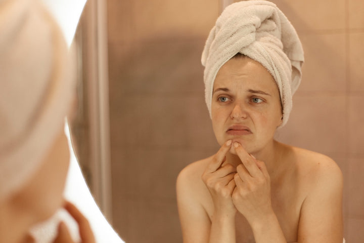 a woman examining her acne in the mirror