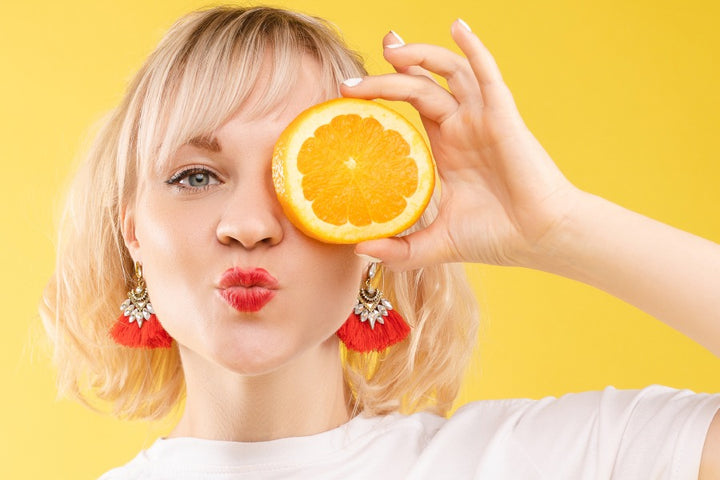 a woman holding half a orange infront of one of her eye