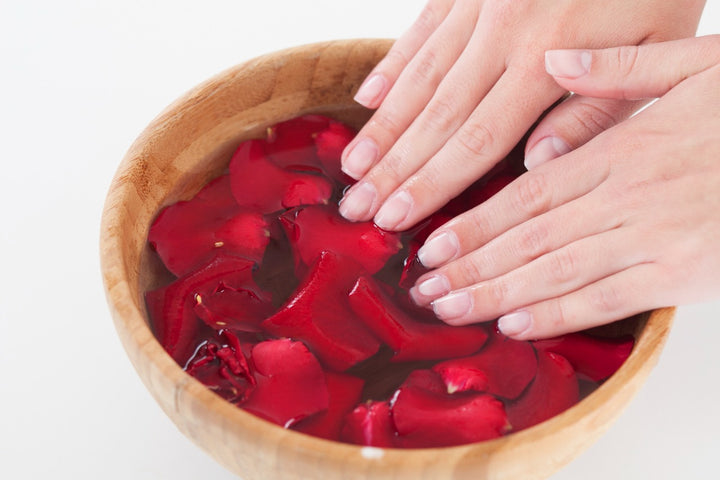 a woman touching a bowl full of rose petals and water