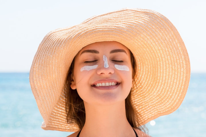 a woman is wearing a cap with closed eyes and has applied sunscreen cream on her face