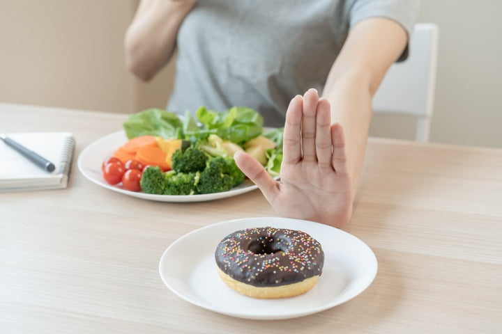 a woman making a sign of saying no using her hands when a plate of donut is offered to her.